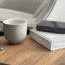 Sobre una mesa, una taza, un mando, un libro.